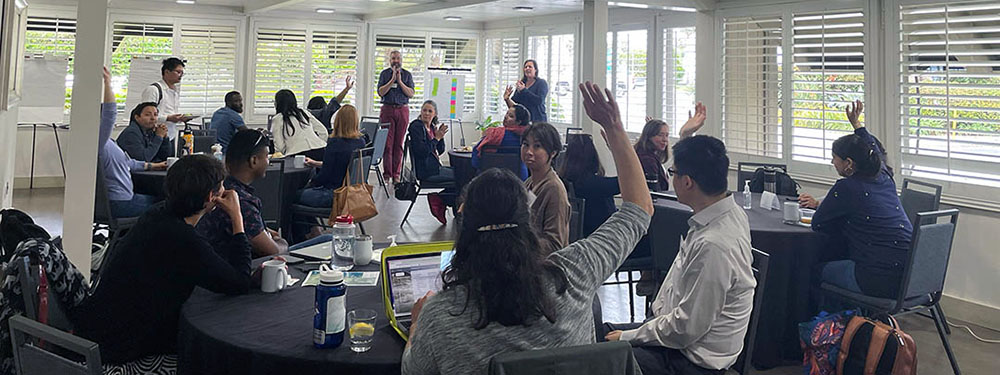 Attendees at a MCTEN Writing Retreat participating in an interactive session indoors, with some raising their hands.