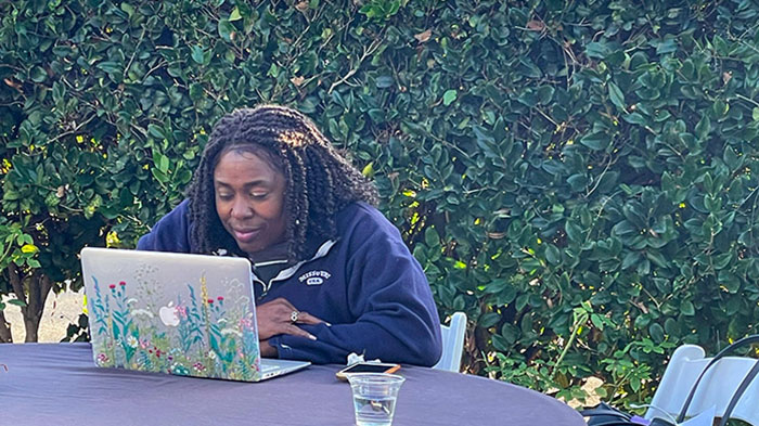 Person working on a laptop outdoors at the MCTEN Writing Retreat, seated at a table surrounded by greenery.